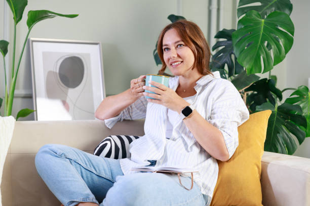 istock Young woman sitting on the couch and drinking coffee 1870201340