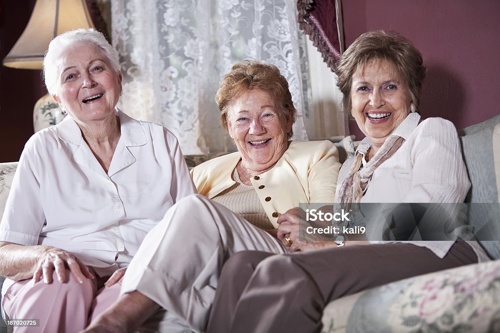 Elderly women on living room sofa Group of senior women (80s) laughing together on living room couch. Laughing Stock Photo