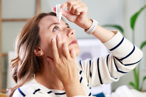 Young woman putting eye drops at home