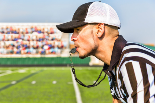 A referee watches with whistle ready during a football game.