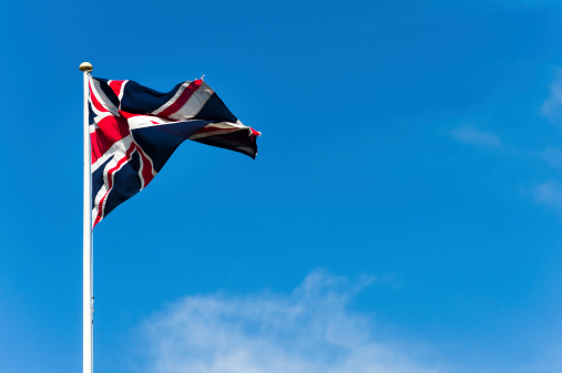 A crumpled Union Jack (flag of United Kingdom) against blue sky on a bright, windy day.