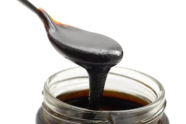 Organic Molasses being scooped out of a jar, shot against a white background.