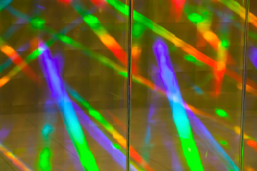 Diffracted and saturated rainbow light colours reflected from a prismatic covering on a wall. A small amount of the surface texture and ripple can be seen in the photo (not to be confused with noise).