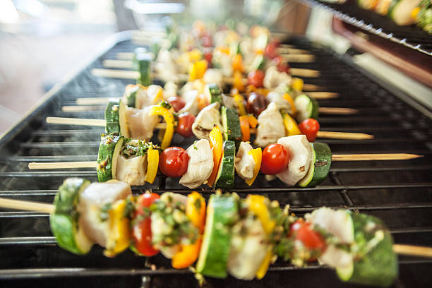 Tasty Kebabs Shishkabobs on Grill with wood skewers, and a medley of food being grilled to perfection in a shallow depth of focus look.  Chicken, pepper, onions, glaze and squash.