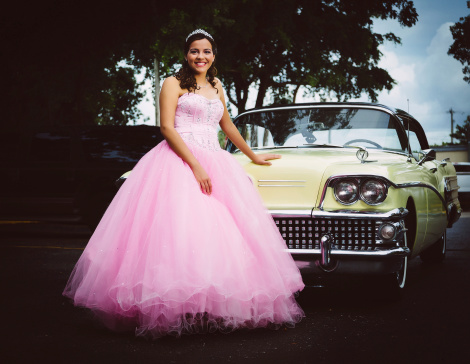 quinceanera wearing a traditional dress posing in front of an american car from the 50s