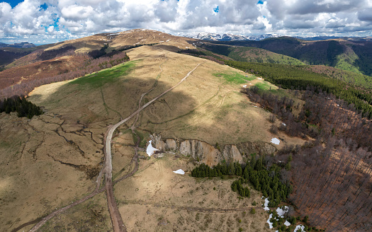 Aerial drone view above Parang Mountains. Springtime, snow still covers the pastures. Clouds are taking over the sky. The beech forest is not blooming yet. Carpathia, Romania. Alpine landscape.