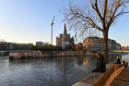 Paris, France-12 17 2023: People on the banks of the Seine river in front of the Notre-Dame Cathedral covered in scaffolding during its reconstruction, Paris, France.