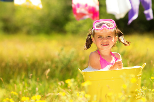 Little girl playing in a metal bathtub with cloths line in background
