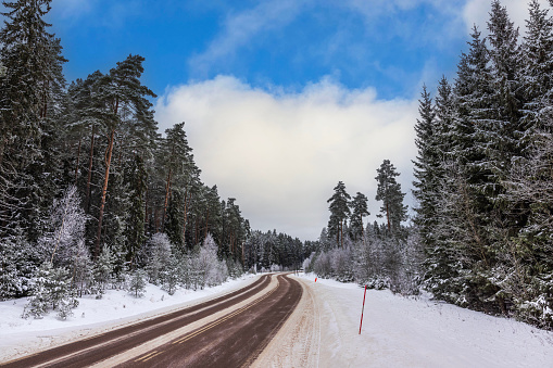 Beautiful view of winter landscape with road passing through forest against backdrop of blue sky with white clouds on frosty day. Sweden.