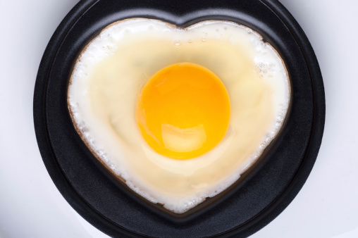 Heart shaped fried eggs with toast in frying pan on wooden table, top view