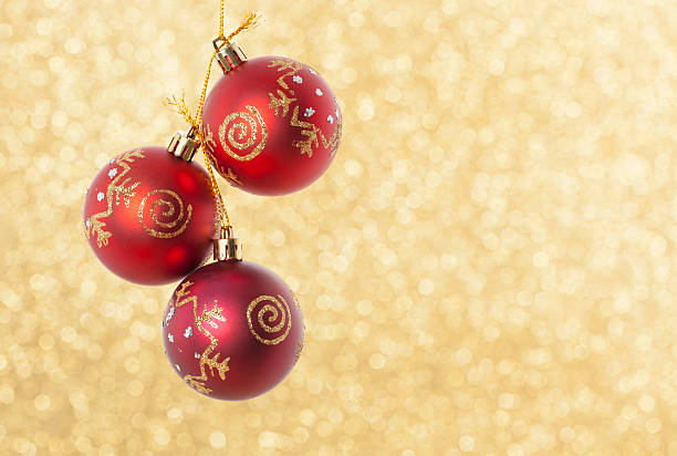 Three Christmas red balls on golden light background.