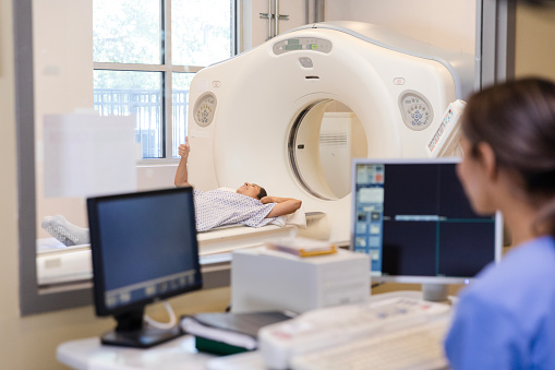 A female radiographer talks with a CT scan patient while in the control room.