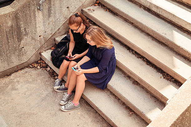 istock Two high school teenagers texting on staircase. 187035293