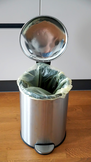 Metallic trash can on the parquet floor in a kitchen near of kitchen furniture