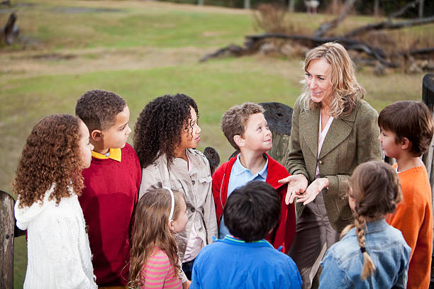 Teacher with group of children at zoo Teacher (50s) with multi-ethnic group of elementary school children at zoo, standing on observation deck overlooking animal exhibit. firld trips  stock pictures, royalty-free photos & images