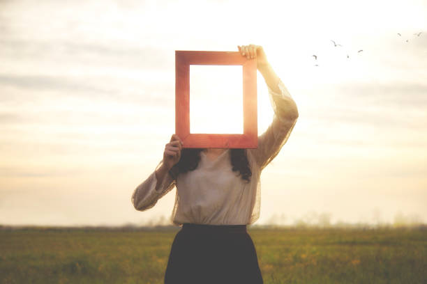 istock woman holds an empty frame that makes her face disappear reflecting the sky, abstract concept 1870375805