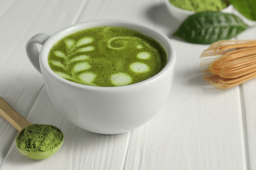Delicious matcha latte and powder on white wooden table, closeup