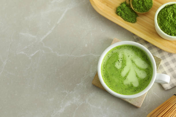 istock Cup of fresh matcha latte and green powder on light grey marble table, flat lay. Space for text 1870377385