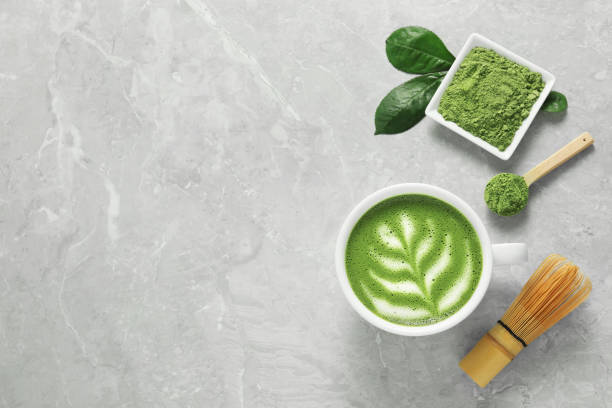 istock Cup of fresh matcha latte, powder and bamboo whisk on grey marble table, flat lay. Space for text 1870377388