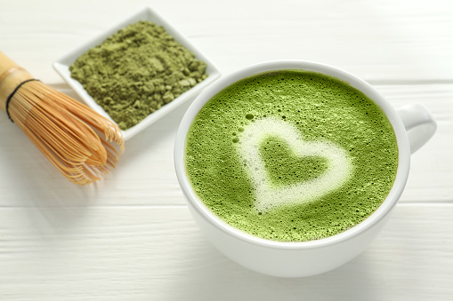Cup of fresh matcha latte on white wooden table, closeup