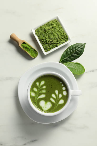 istock Delicious matcha latte, powder and leaves on white marble table, flat lay 1870377392