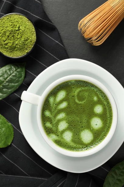 istock Delicious matcha latte, powder, leaves and whisk on dark table, flat lay 1870379468
