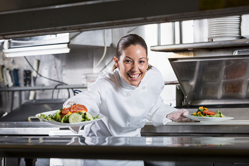 Female Hispanic chef (30s) in commercial kitchen, preparing gourmet salad.