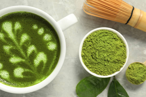 istock Delicious matcha latte, powder, leaves and whisk on grey textured table, flat lay 1870379476