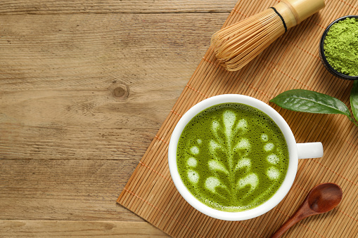 Delicious matcha latte, powder, spoon and whisk on wooden table, top view. Space for text
