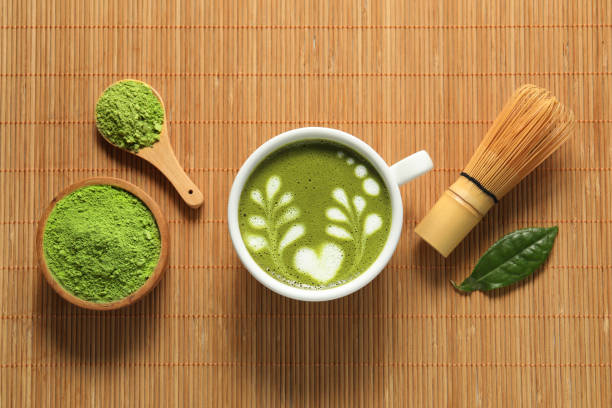 istock Delicious matcha latte, powder, leaf and whisk on bamboo mat, flat lay 1870380546