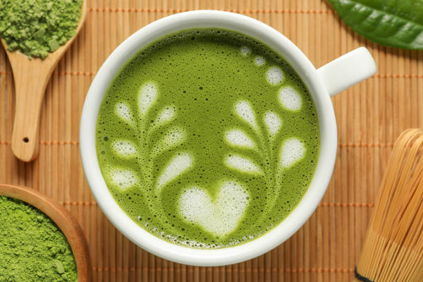 istock Delicious matcha latte, powder, leaf and whisk on bamboo mat, flat lay 1870381064