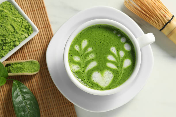 istock Delicious matcha latte, powder, leaf and whisk on white table, flat lay 1870381070