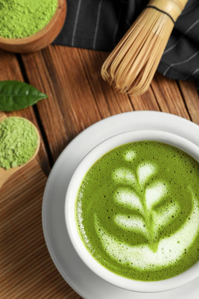 istock Delicious matcha latte, powder, leaf and whisk on wooden table, flat lay 1870381078