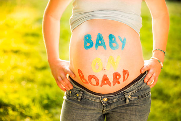 Pregnant Woman With Text baby On Board On Her Belly Standing At Park