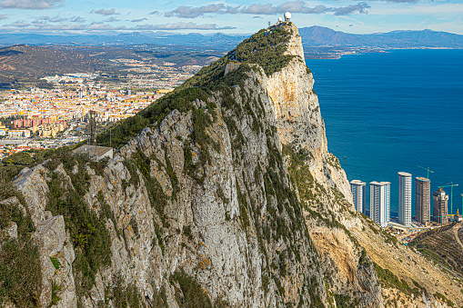 Gibraltar - 11th November 2023: View of the peak of the Rock of Gibraltar, including the sheer limestone cliff and the skyscrapers at Hassan Centenary Terrace on the Eastside then looking beyond the Rock to La Linea and beyond in Spain.