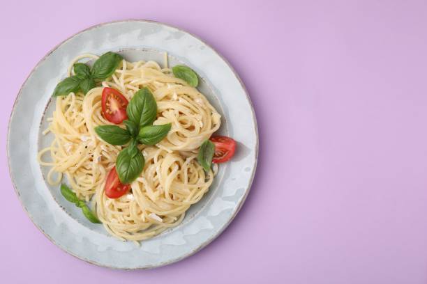 istock Delicious pasta with brie cheese, tomatoes and basil leaves on violet background, top view. Space for text 1870396257