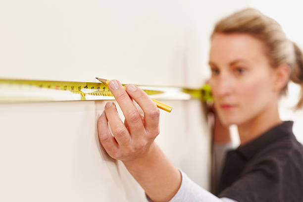 Young female worker marking distance on wall