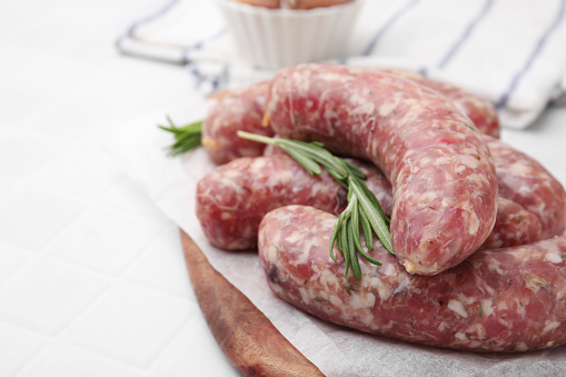 Raw homemade sausages and rosemary on white table, closeup. Space for text