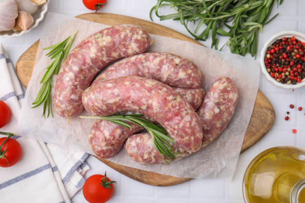 istock Raw homemade sausages and different products on white tiled table, flat lay 1870411322
