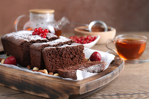 Tasty chocolate sponge cake with nuts and berries on wooden table, closeup