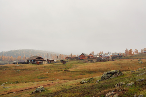 Small village on a rocky hill under the mountain in fog. Real rural life. Golden autumn landscape of snowy foggy morning in the village of Belyashi, Russia
