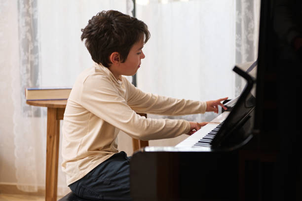istock Caucasian schoolboy touching white and black keys, performing classical musical composition while playing piano at home 1870449107