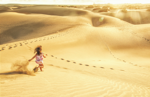5 year old girl running down the dunes into the sunset and towards the town of Maspalomas, Gran Canaria