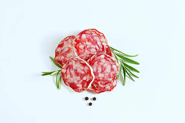 french dried salami slices with fresh rosemary and peppercorns on white background