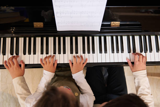 istock Top view of children hands on piano keyboard, touching white and black keys while playing music on grand piano 1870462320