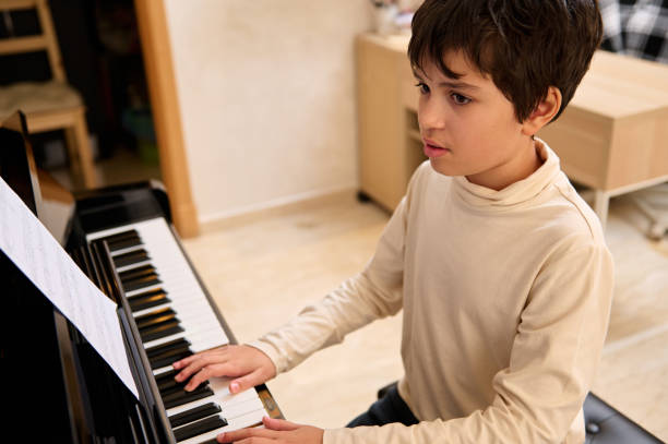 istock Handsome school child boy touching black and white keys, preforming classical melody during music lesson 1870464961