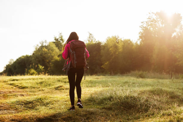 istock Back view of woman walking with backpack on meadow 1870466596