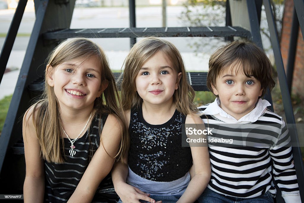 Color Image of Two Sisters and Their Little Brother Color image of two little girls, and one little boy, sitting together inside and looking at the camera. 10-11 Years Stock Photo