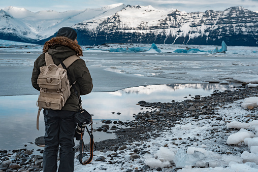 Traveling to Iceland, man with backpack and camera standing on the shore and enjoying view on Jokulsarlon Glacier Lagoon, extreme winter vacation