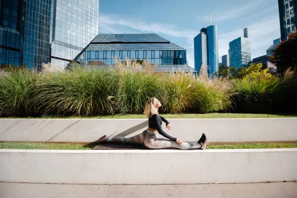 Blonde woman doing leg-split and warming up muscles at the sunny street alone. Sport and recreation concept